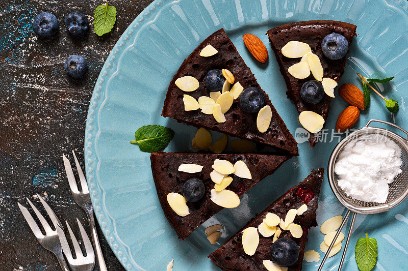 蓝色盘子里放着蓝莓和樱桃的巧克力布朗尼。