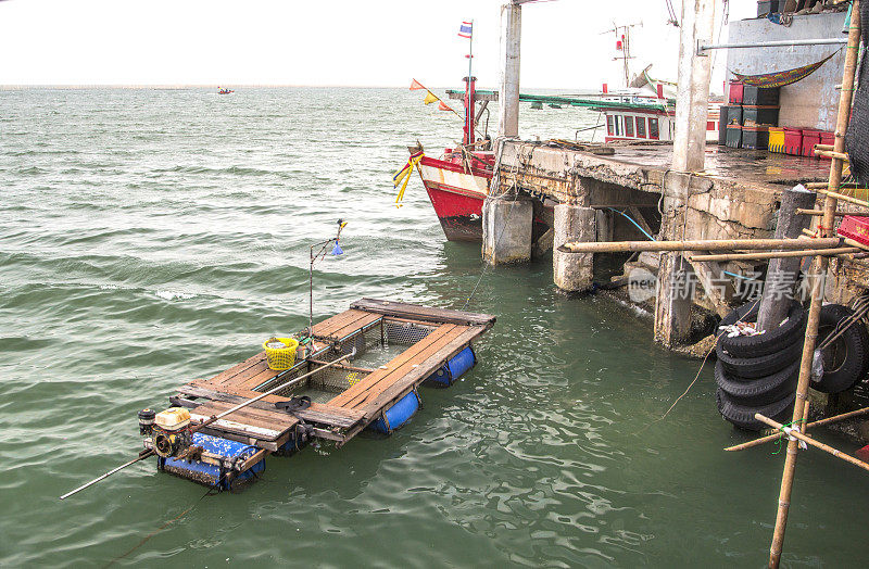 摇摇欲坠的码头上有五颜六色的渔船。带发动机和帆的筏子在海里。泰国,亚洲