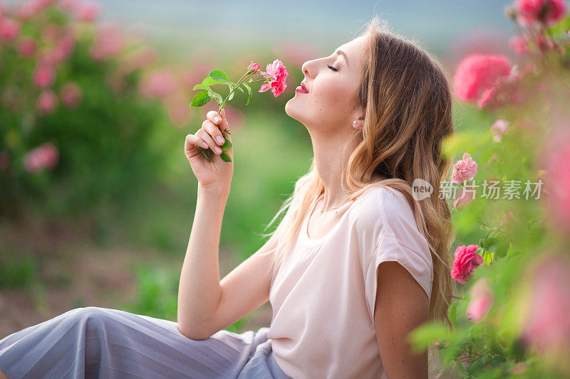 美丽的年轻女孩穿着休闲的衣服休息在一个粉红色的花玫瑰花园
