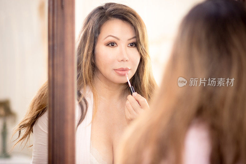 美丽的亚洲女人看着古老的镜子，涂着唇彩