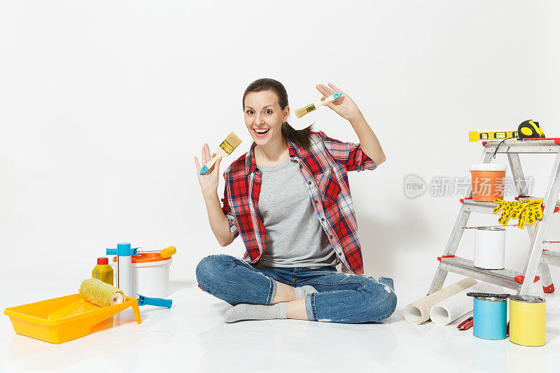 漂亮的女人穿着便服坐在地板上用刷子，仪器为装修公寓房间隔离的白色背景。壁纸配件用于粘漆工具。修理家里的概念