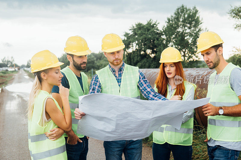 年轻建筑工人在建筑工地使用蓝图