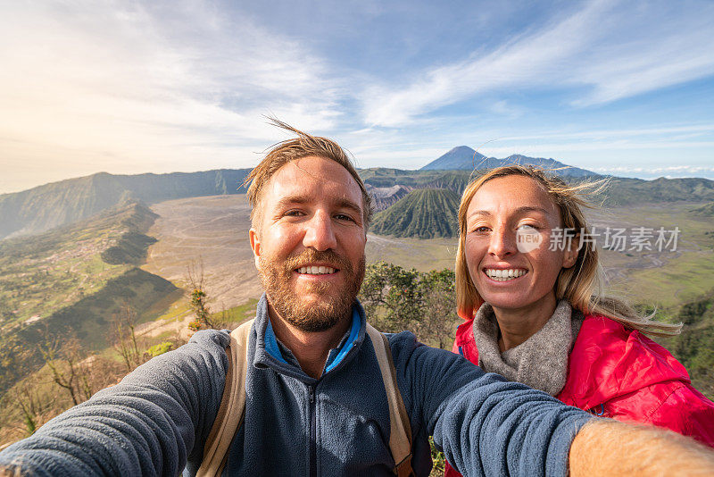 年轻的夫妇徒步旅行自拍在山顶与布罗莫火山的观点-人们旅行冒险的概念