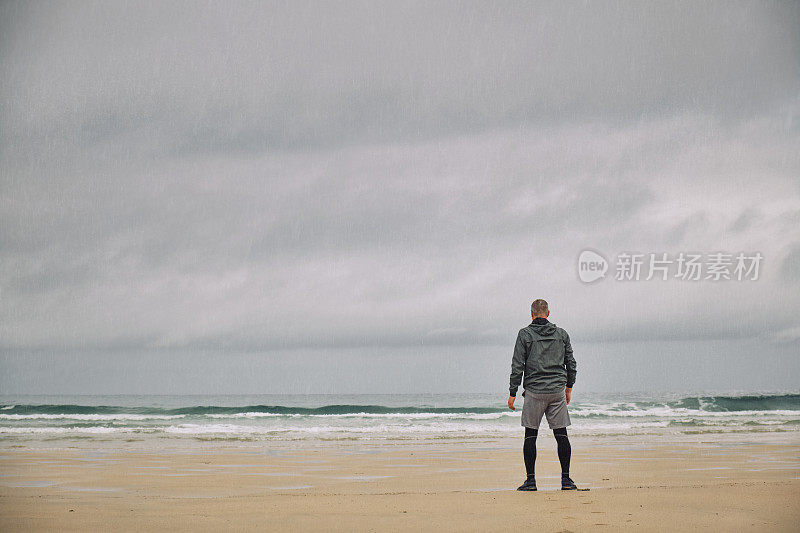 一名男子在雨中站在阴沉沉的海滩上晨跑。
