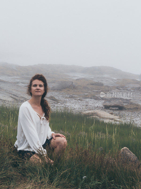 优雅美丽的女人独自坐在岩石多雾的海岸