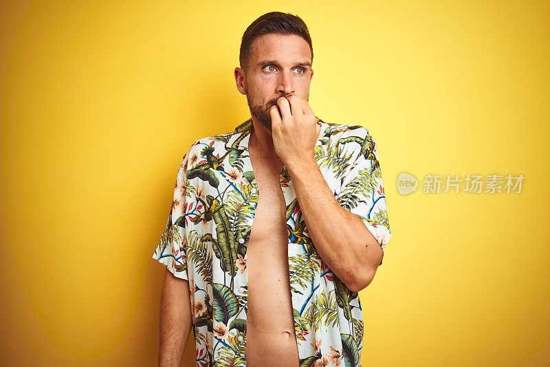 英俊的男人穿着夏天夏威夷花衬衫在黄色孤立的背景看起来紧张和紧张与手在嘴咬指甲。焦虑的问题。