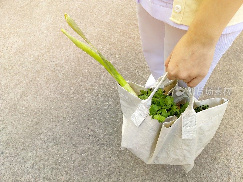 为了减少全球变暖，年轻女性早上在新鲜市场用可回收袋购买蔬菜。