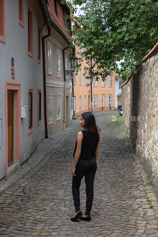 漂亮的30岁混血女人站在标志性的老窄鹅卵石街-布拉格
