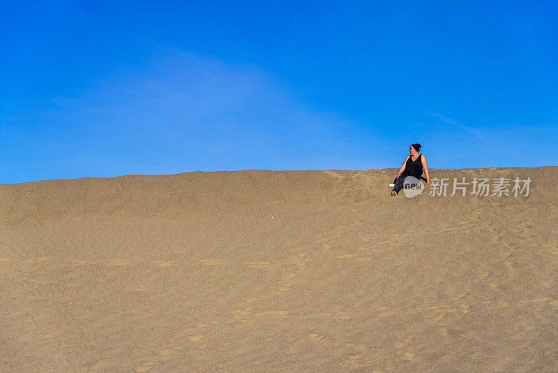 一名妇女坐在和休息在沙丘上，梅斯奎特平原，死亡谷，加利福尼亚州。