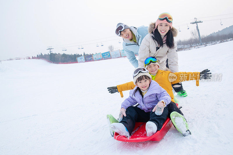 滑雪场上父母推着坐在雪上滑板的孩子们