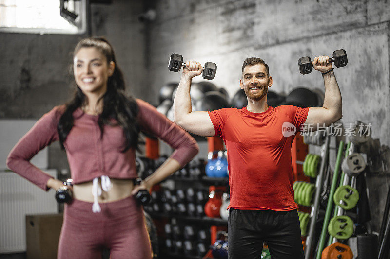 在年轻女性健身教练的帮助下，年轻的运动男子正在健身房用哑铃进行重量训练