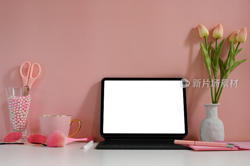 一个白色空白屏幕的平板电脑被放置在一个被各种设备包围的办公桌上。