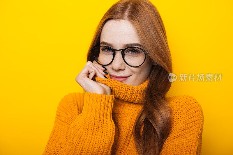 一个白人女人的近距离照片读头发和雀斑戴眼镜和橙色毛衣在黄色的背景