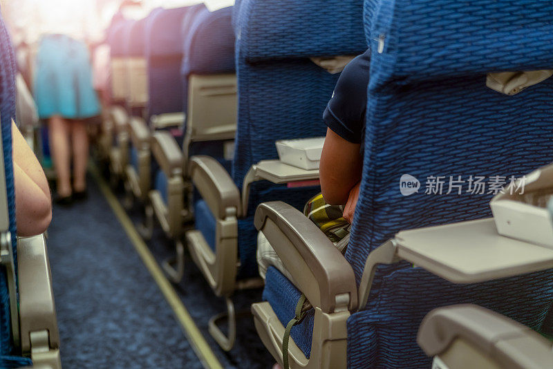 商务飞机经济舱座位内的乘客。飞机客舱内饰。模糊女乘务员或空中小姐在飞机过道上为乘客服务。人们乘坐拥挤的飞机旅行。