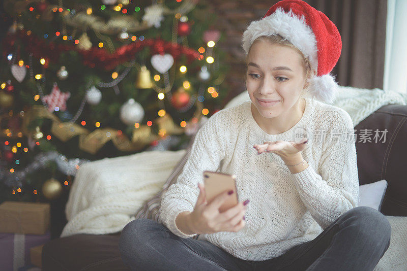 年轻女子在圣诞节室内与智能手机(网上约会)