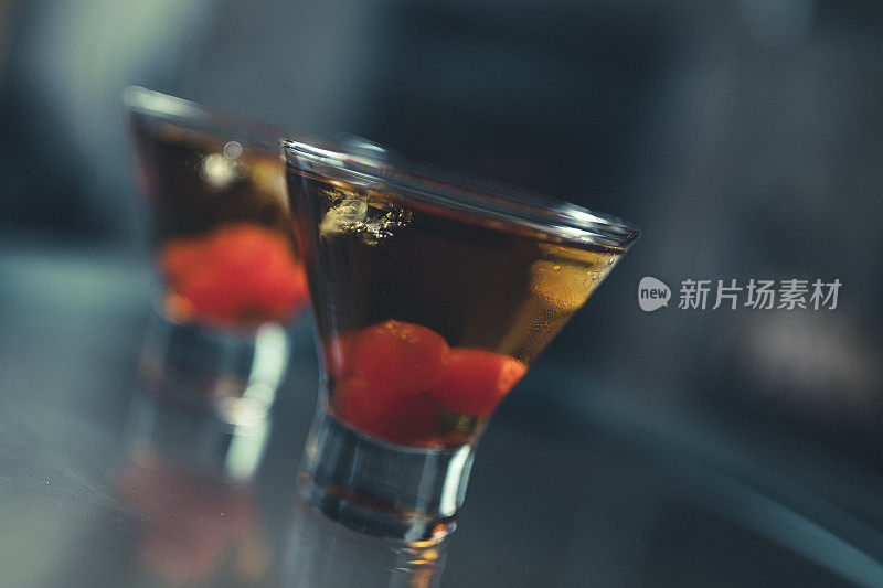在一张玻璃桌子上，两个美味的曼哈顿鸡尾酒的特写镜头，也被称为曼哈顿鸡尾酒，配以樱桃。