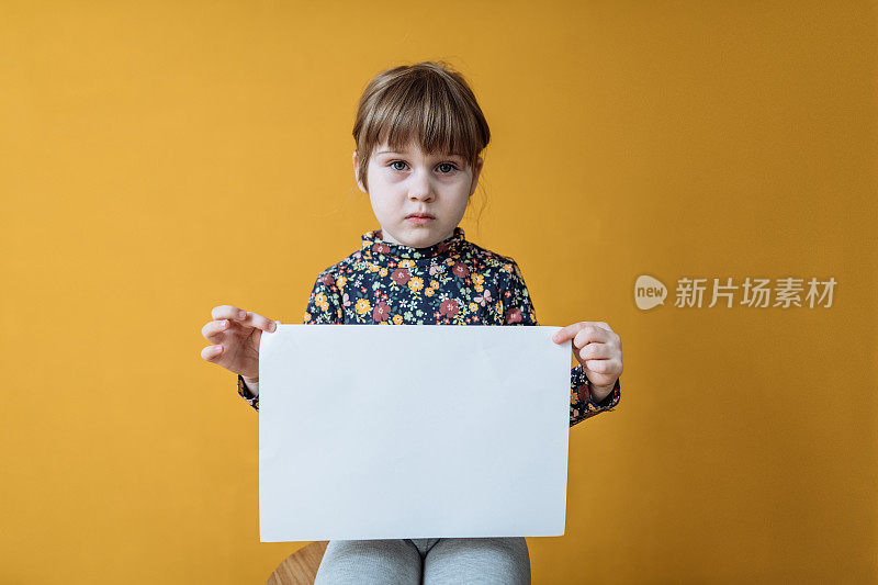 四岁女孩的工作室肖像，带着悲伤的脸拿着空白纸。适合儿童虐待或童工信息