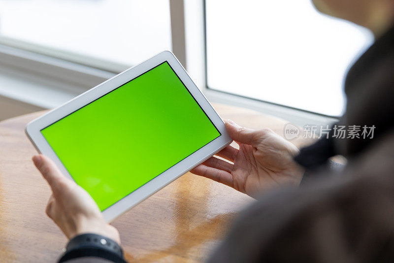 女人的手拿着色度键绿色屏幕的数字平板电脑在办公室的特写