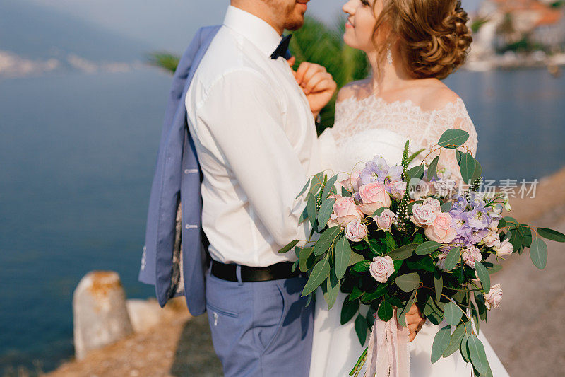 新娘和新郎站在码头上拥抱，新娘手里拿着一束花，特写