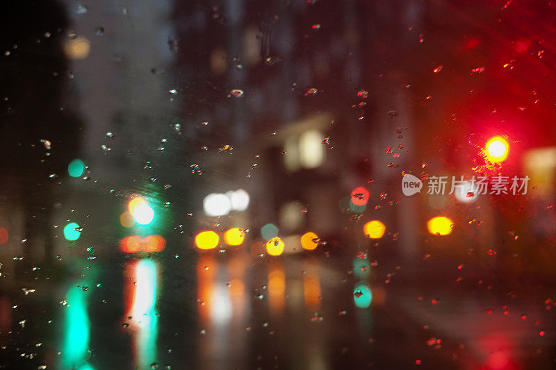 失去焦点的雨天街景，五颜六色的交通灯，挡风玻璃上的雨滴在前景。