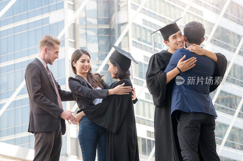 人们怀着快乐和感恩的心情，带着毕业礼服和毕业帽，与父母和朋友站在一起，在户外现代城市空间里欢快地打招呼。