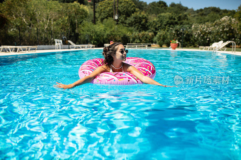 在一个炎热的夏天，一个美丽的女孩在一个充气甜甜圈的游泳池里玩得很开心