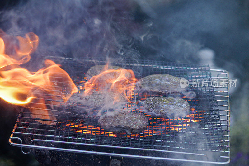 烟雾的便携式火焰，在花园里的木炭烧烤，在户外的金属烤架上烹饪的汉堡，烟雾，聚焦前景