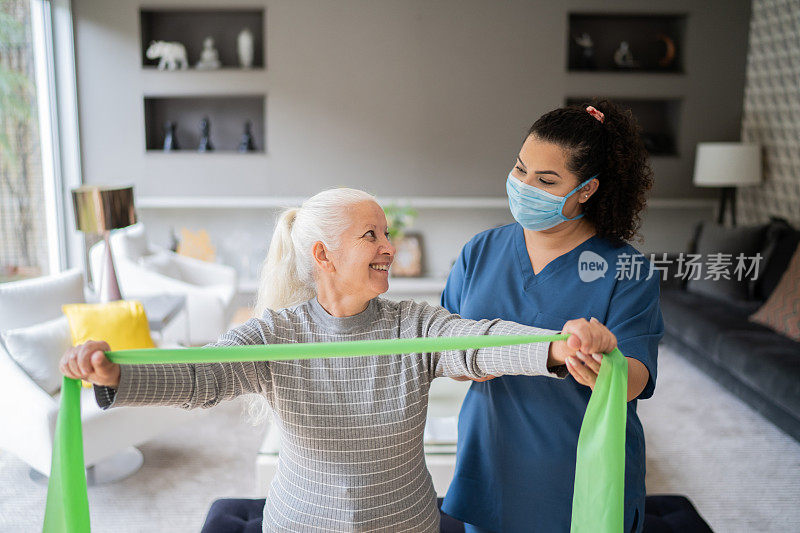 资深妇女在物理治疗师的支持下使用阻力带进行运动-佩戴防护口罩