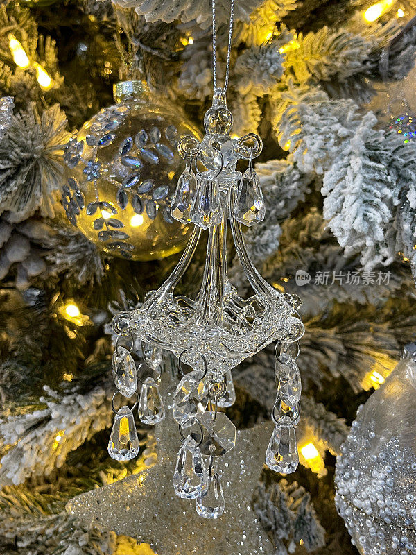 形象的玻璃枝形吊灯装饰挂在人造圣诞树的树枝上，云杉针上覆盖着人造的雪花喷雾，模糊的白色精灵灯背景