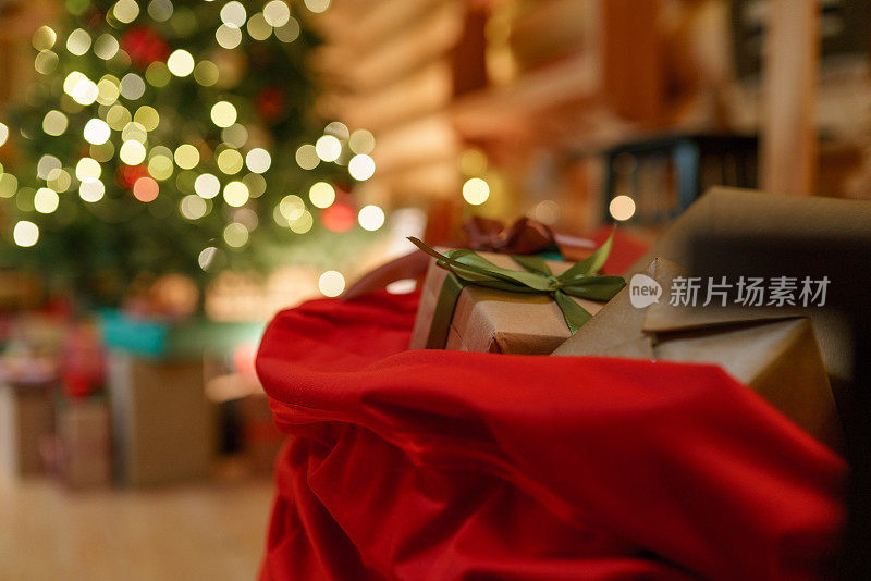 一幅圣诞画，装饰模糊的圣诞树和圣诞老人的包和礼物在前景的焦点