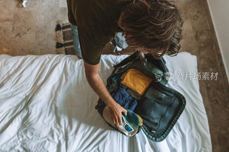 男性旅行者打包旅行的俯视图，把衣服放在行李袋里