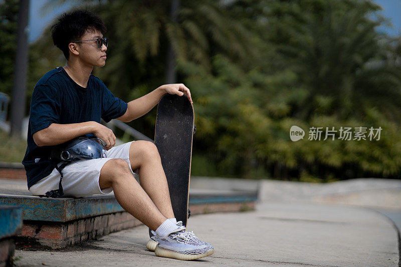 亚洲中国少年在滑板公园休息