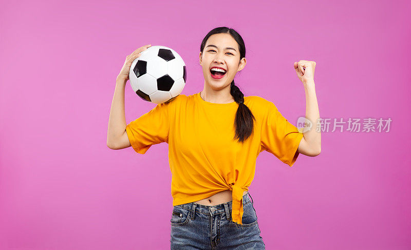 快乐的亚洲年轻女子在孤立的粉红色背景下拿着足球，足球和人，国际足联世界杯的概念