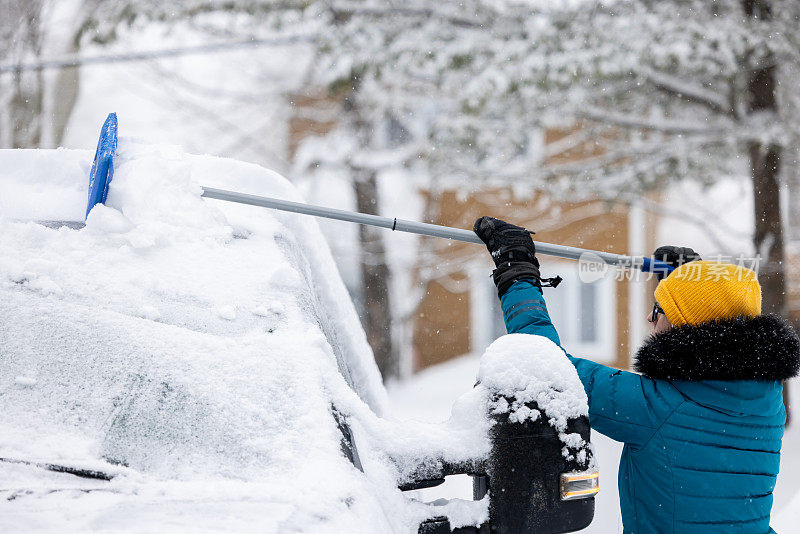 一名年轻女子在暴风雪后清理车上的积雪