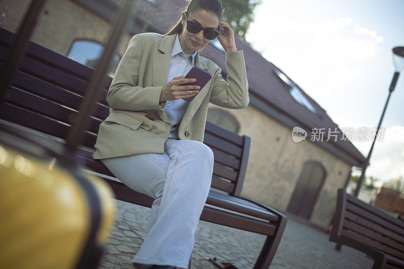 坐在长凳上，远离马路休息时，游客使用手机。
