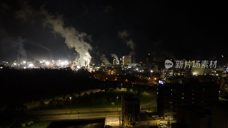 夜间城市鸟瞰图，背景是钢铁发电厂排放的烟雾