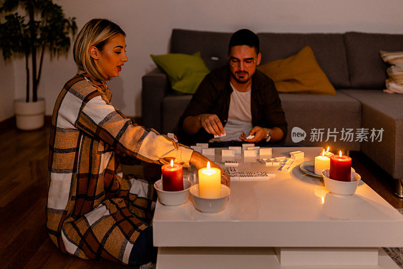 在一次精力充沛的危机中，一对年轻夫妇在黑暗中点着蜡烛玩多米诺骨牌。