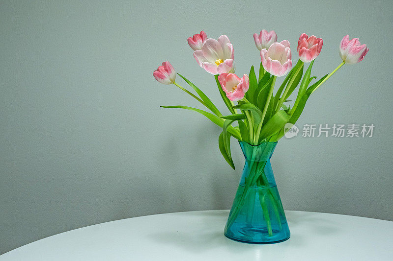 白色桌子上的透明玻璃花瓶里插着一束粉红色的郁金香。