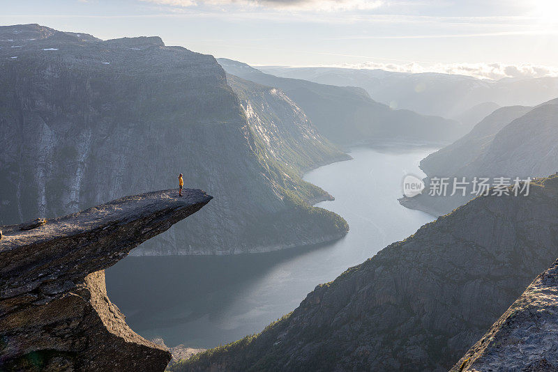 一名女徒步旅行者站在巨魔之舌(trollltunga)著名的岩石上，俯瞰湖面上的山谷全景，是挪威著名的探险之旅