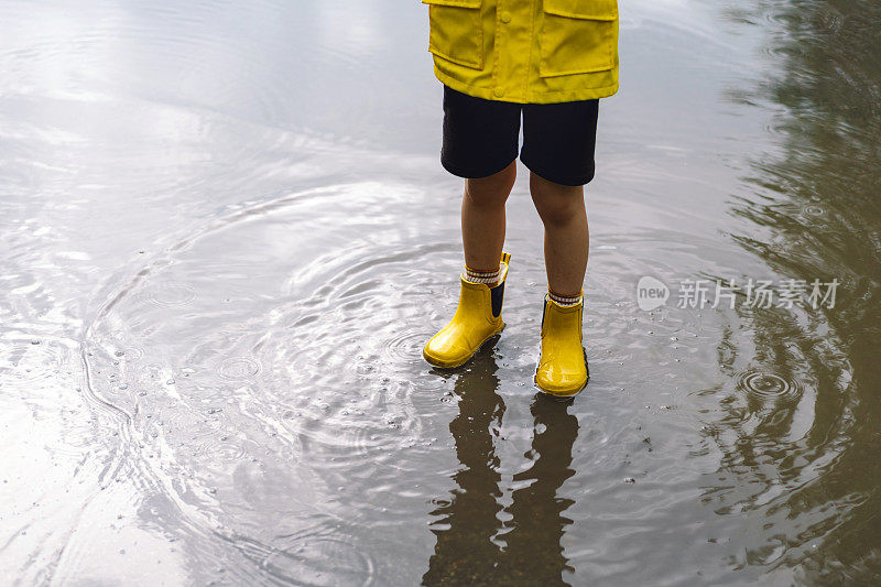 春天的一天，可爱的小男孩穿着雨衣和胶靴走过水坑