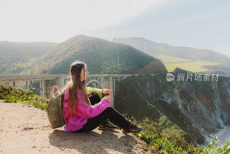 一名女子旅行者放松与风景秀丽的比克斯比溪桥在大苏尔，加利福尼亚