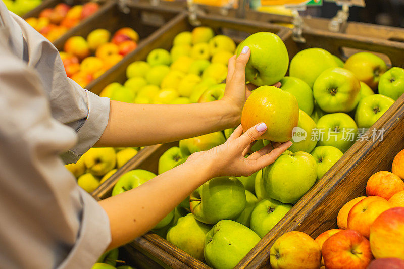 年轻的金发女郎在水果区挑选苹果。秋季市场。素食主义。健康食品。选择。购物