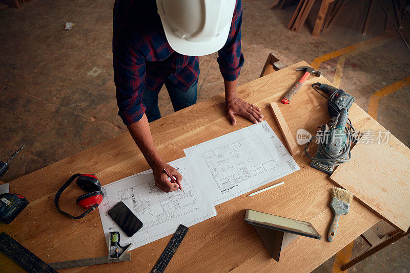木工工厂数码平板旁，戴安全帽的中年男子在纸上写字的高视角