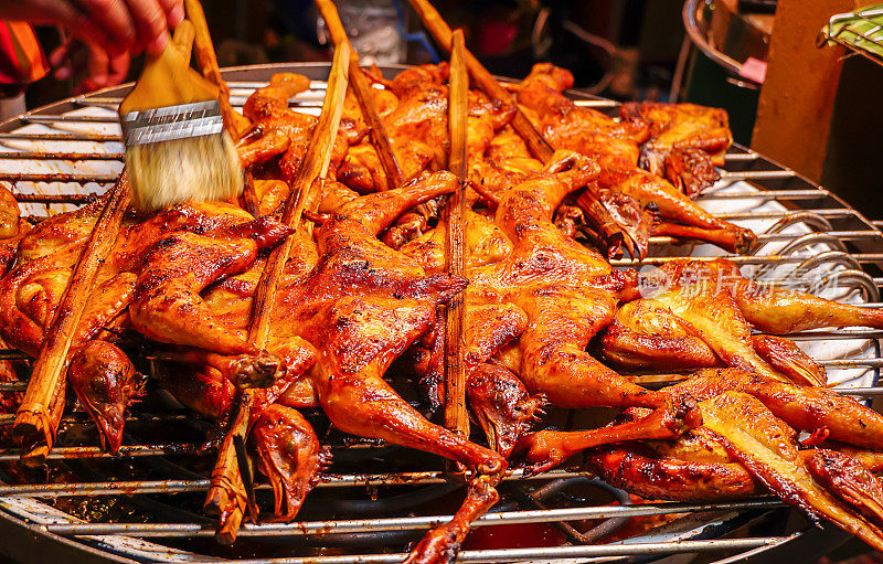 用竹签在炉子上用木炭烤鸡翅，卖主用手把酱汁刷在鸡上。烤鸡烧烤特写。美味的亚洲料理。