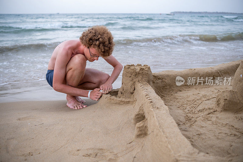 一个大男孩正在沙滩上堆沙堡。