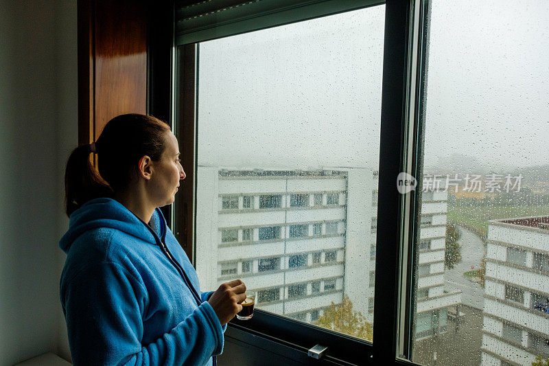 下雨天，一个手里拿着咖啡的女人望着窗外