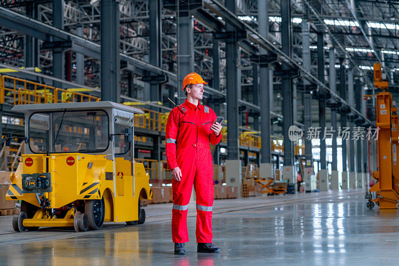专业技术工人站在工厂卡车附近，手持手机，也期待在电气或地铁列车工厂。