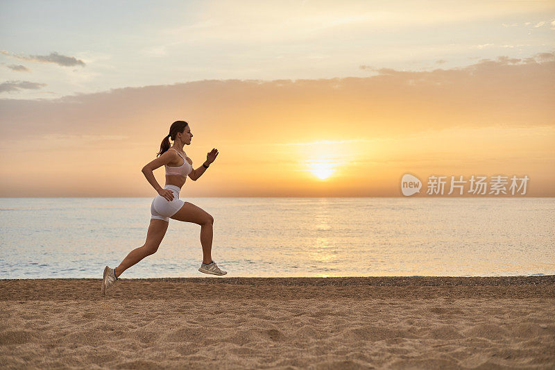 一个健康的女人在海边迎着明亮的日出慢跑