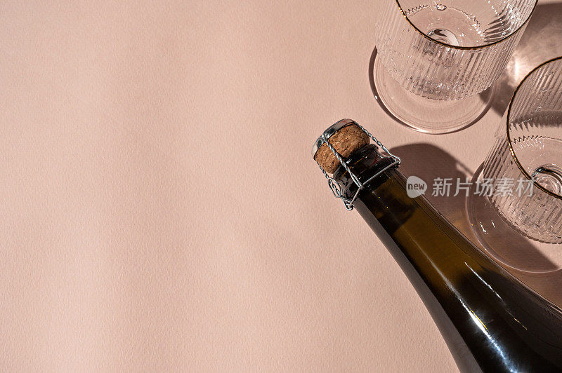 瓶与起泡酒和葡萄酒杯中性桃色背景与刺眼的阳光阴影，最小的节日庆祝活动与酒精饮料的概念