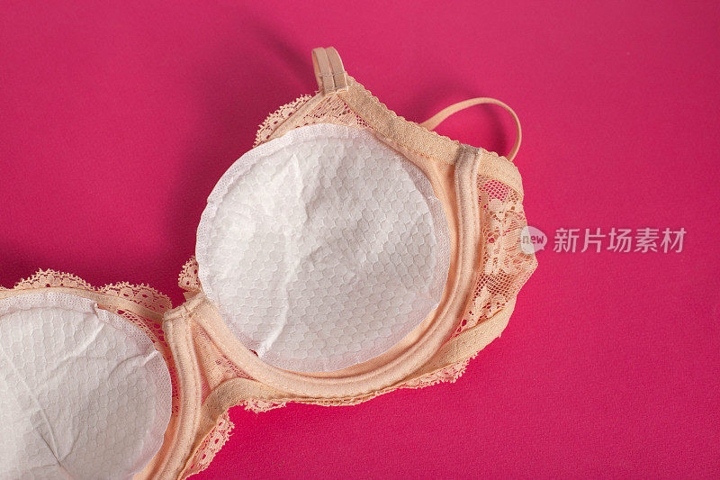 一种女性胸罩，衬里防止乳汁从哺乳妇女的乳房流出，背景为粉红色。
